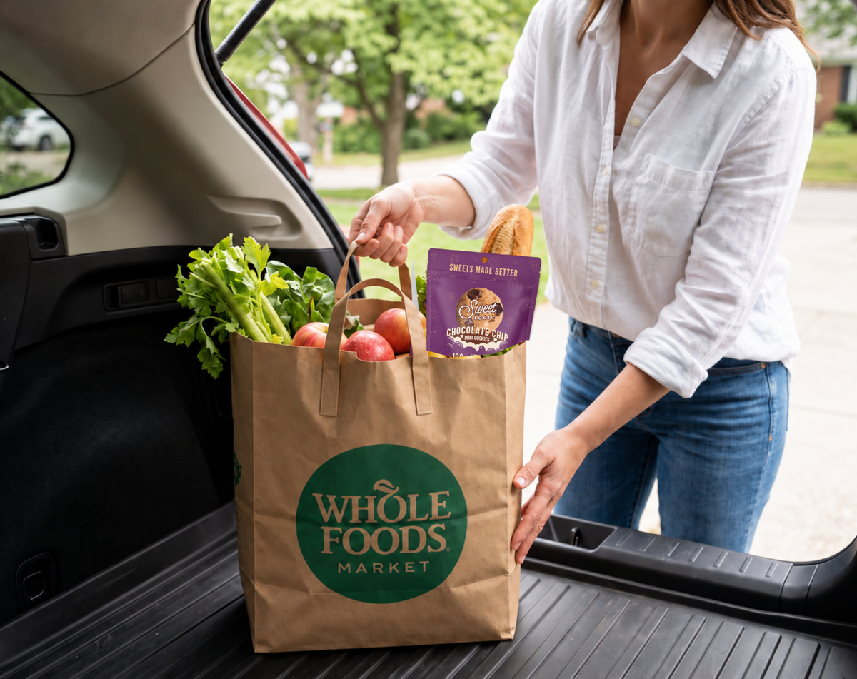 A Whole Foods Market bag with Sweet Logic Chocolate Chip cookies being loaded into a car